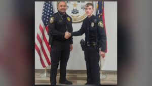 Roanoke Rapids Police Chief Bobby Martin shaking hands with newly sworn-in officer Matthew Simon in front of American and North Carolina flags